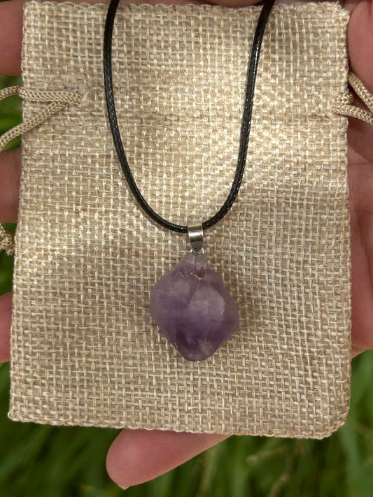 small raw amethyst pendant with silver pendant attachment and black cord necklace on hessian jewellery bag