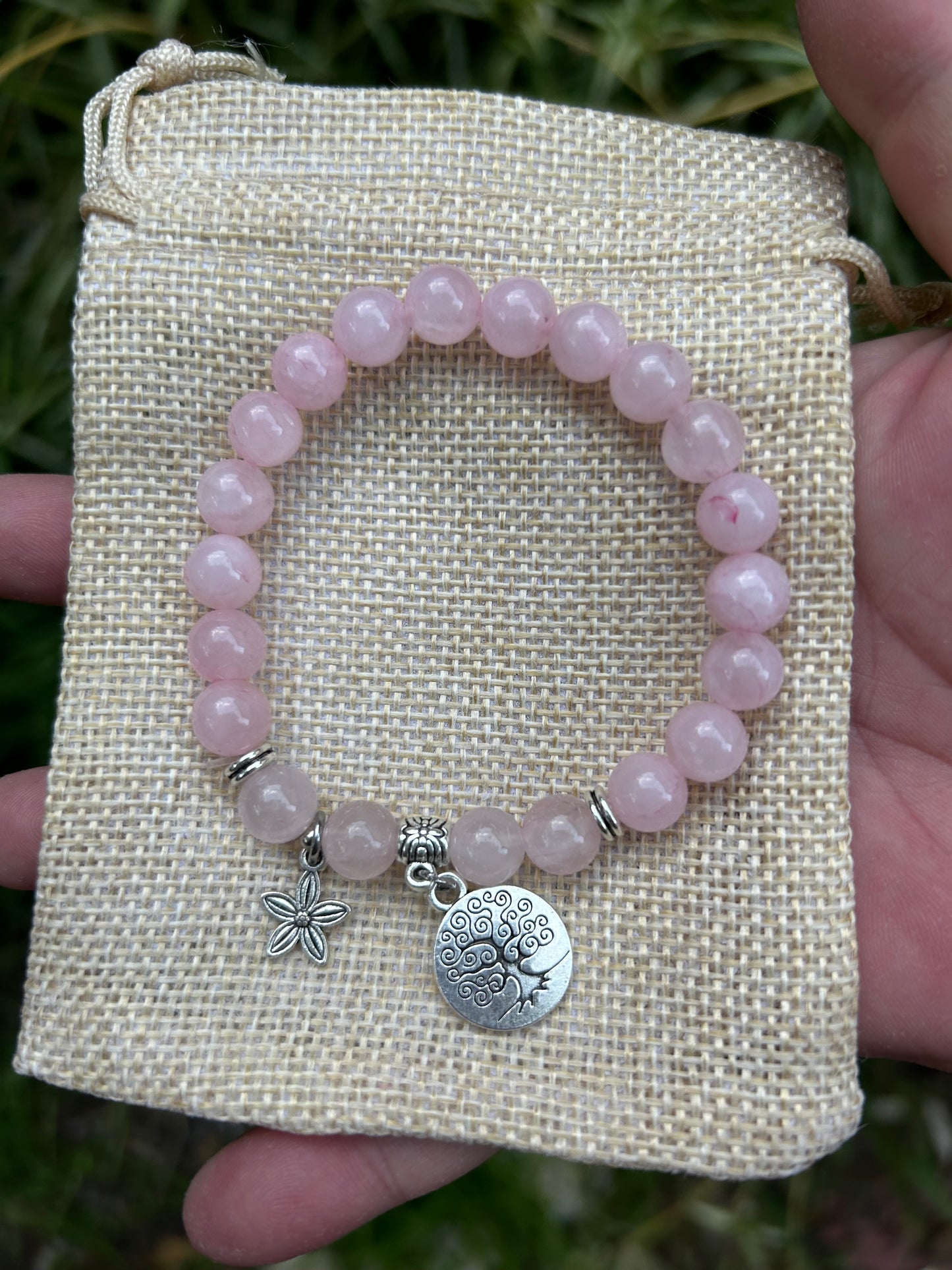 Polished rose quartz bead bracelet with silver detail and flower and tree of life charms on hessian jewellery bag