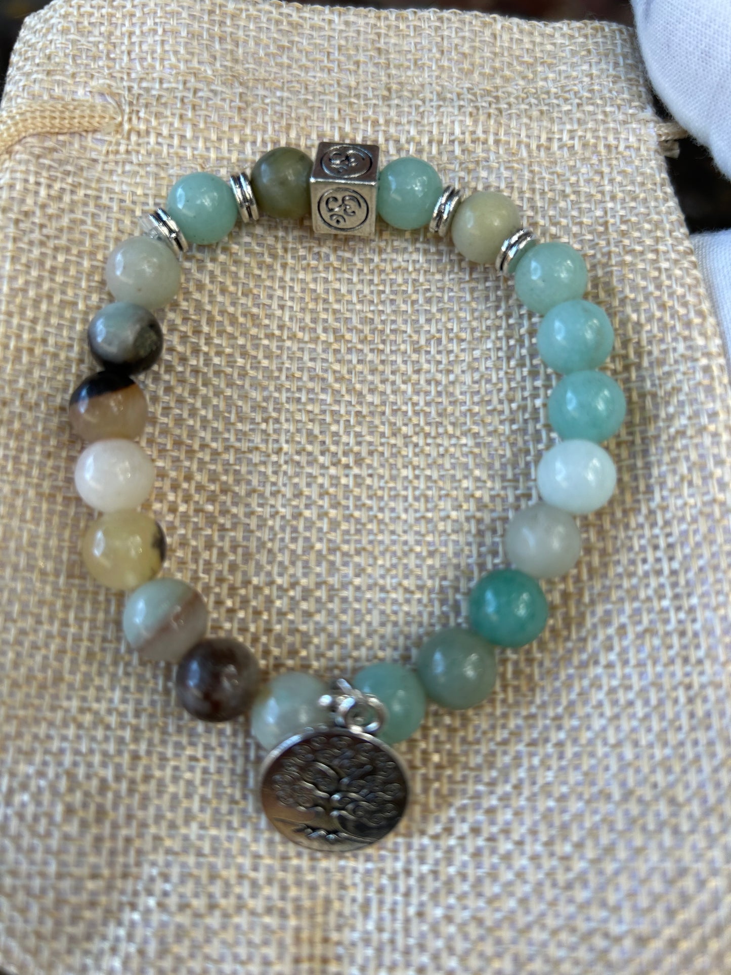 Flower amazonite green tones polished bead bracelet with silver om symbol and round tree of life charm on hessian jewellery bag