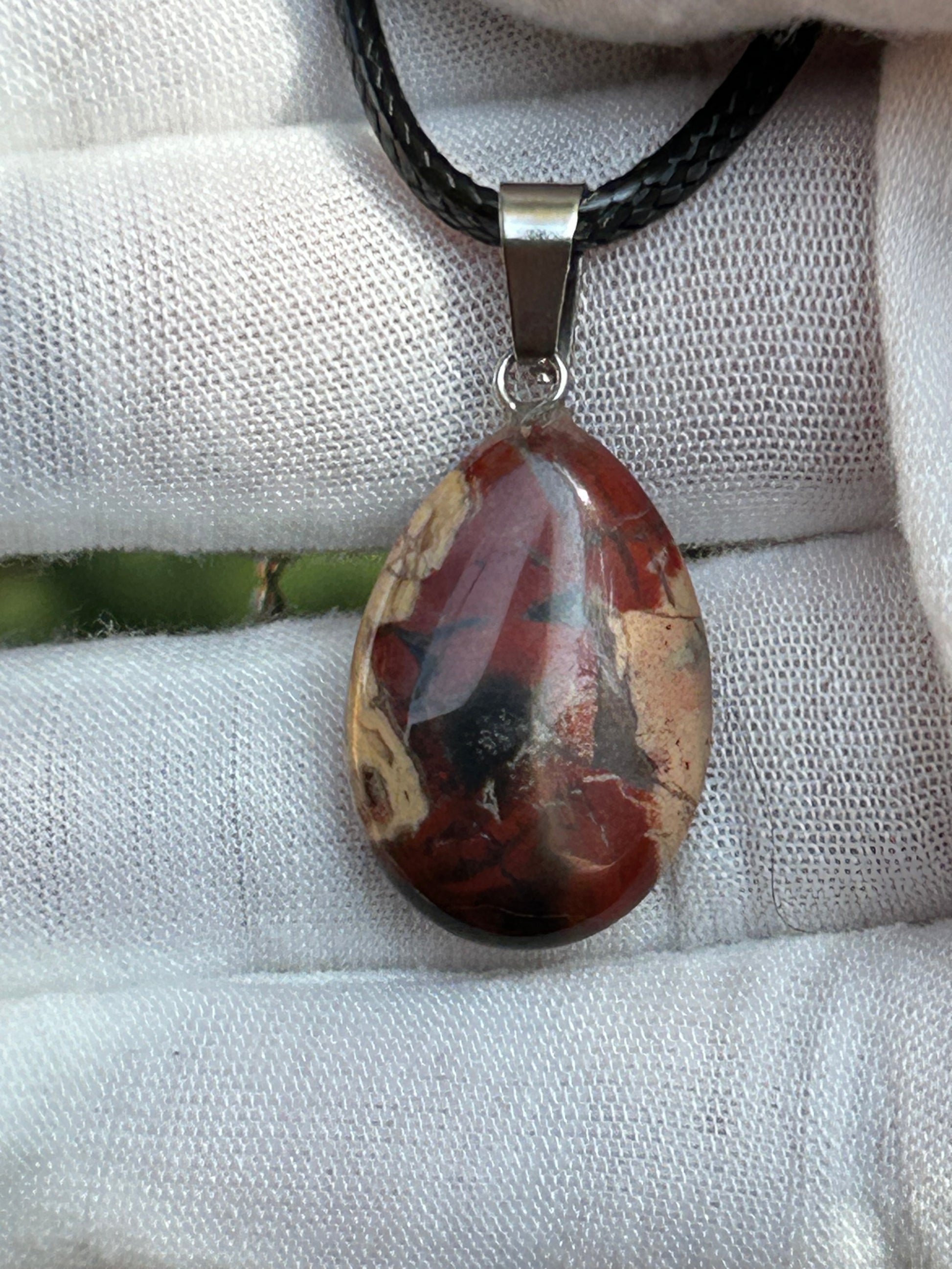 red jasper rain drop shaped pendant with silver pendant attachment and black cord necklace